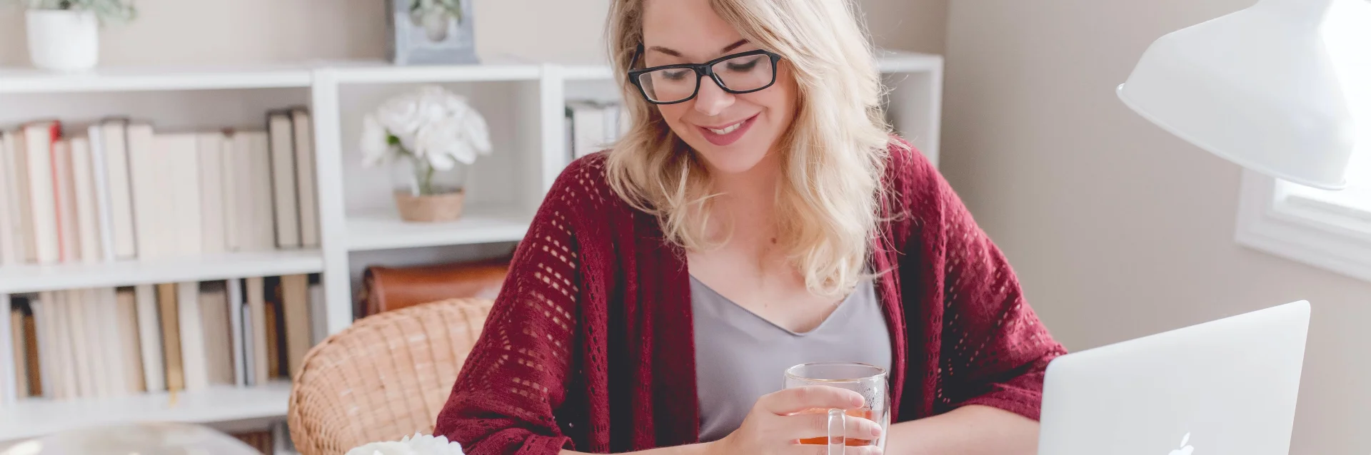 Lächelnde blonde Frau in einem Büro mit einem heißen Getränk in der Hand.