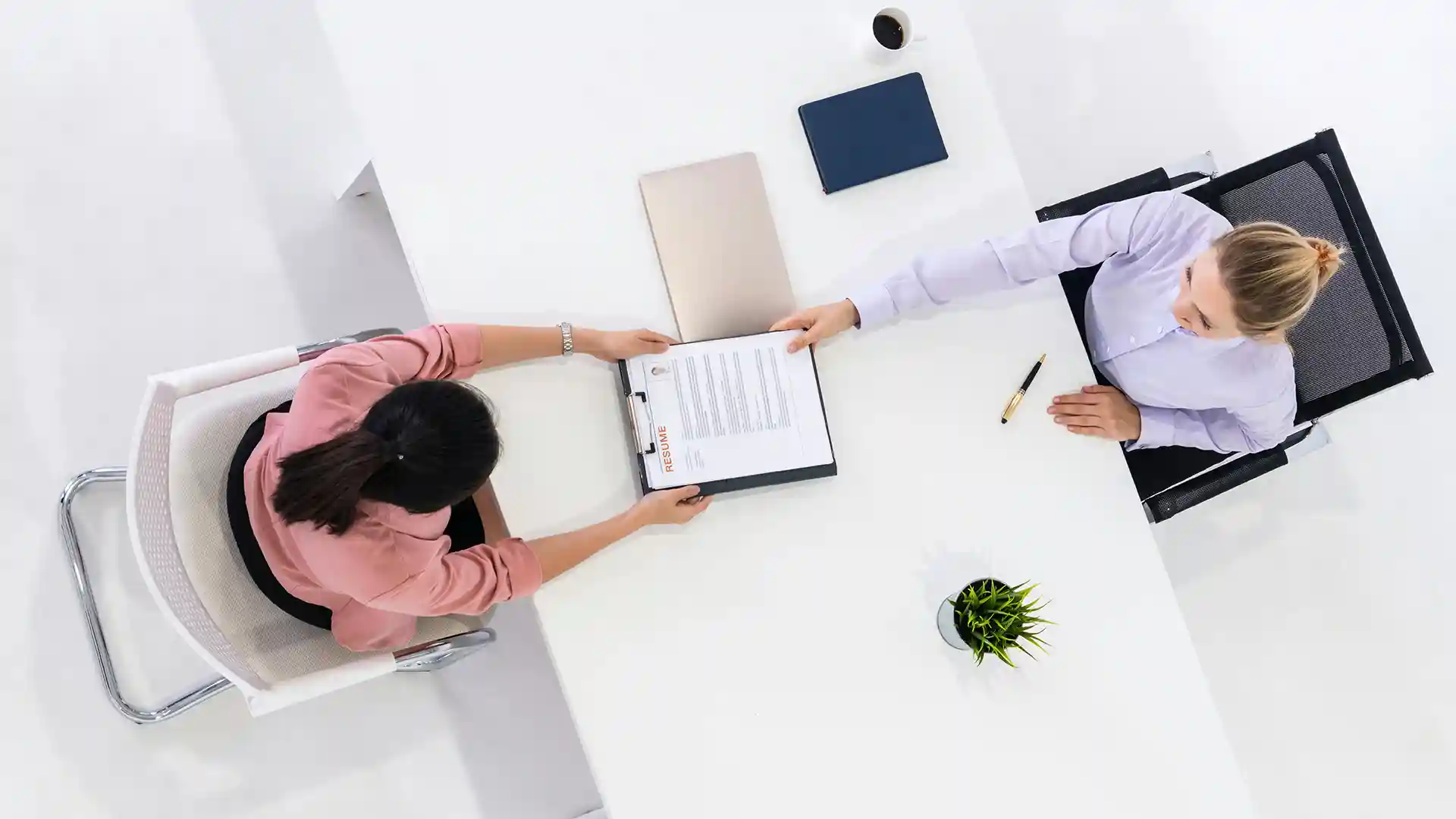 Two women sitting at a white office desk.